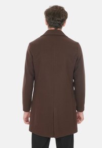 Cappotto in lana marrone con un fit su misura, revers a punta e spacco centrale dietro, mostrato da dietro con un design pulito e minimalista.