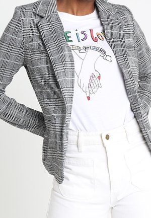 Person iført sort-hvid ternet blazer over hvid T-shirt med to hænder, der holder hinanden, med teksten "Love is Love" i farverige bogstaver.