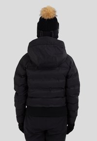 Svart puffjacka med huva, med ribbat fåll och muddar. Parat med en svart mössa prydd med en beige faux fur pom-pom.