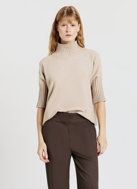 Beige Rollkragenpullover mit kurzen, gerippten Ärmeln; weiche Textur. Kombiniert mit dunkelbraunen, maßgeschneiderten Hosen; einfaches und schlankes Design.