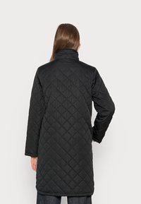 Svart vadderad lång kappa med hög krage, prydd med ett diamantmönster och långa ärmar. Slät textur som definierar modern ytterklädesdesign.