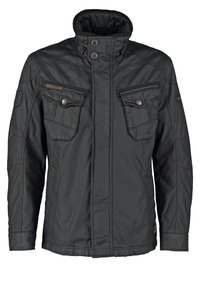 Veste décontractée noire avec col montant, deux poches poitrine boutonnées, manches longues et coutures visibles.