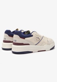 Béžové kožené tenisky s námornícko modrými sieťovinovými akcentmi, bielymi podrážkami a bordovými detailmi. Na boku logo Lacoste, číslo štýlu 933.