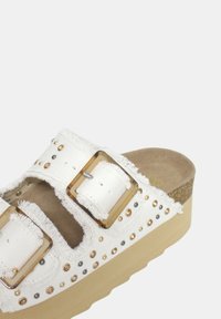 Sandalias de plataforma blancas con correas de lona deshilachadas, hebillas en tono dorado, remaches metálicos y una suela texturizada de color beige.