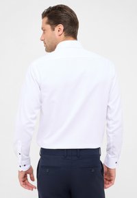 Witte longsleeve shirt met een klassieke kraag, voorzien van een textuurbeschermer en donkere knoopaccenten op de manchetten, gecombineerd met marineblauwe broek.
