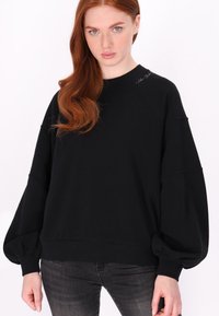 Czarna bawełniana bluza z oversize'owymi balonowymi rękawami, ściągaczami przy mankietach i dolnej krawędzi, z subtelnym logo na ramieniu.