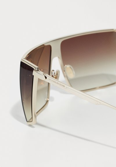 Lunettes de soleil dorées avec de grandes montures rectangulaires et des verres dégradés marron. Présente des éléments de marque gravés sur la branche et un design élégant.