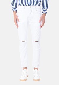 Jeans in denim bianco con ginocchia strappate, slim fit, design a cinque tasche, orli arrotolati, abbinati a sneakers bianche.