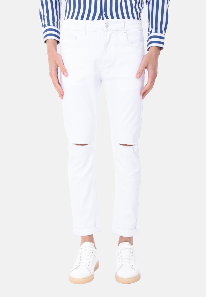 Jeans in denim bianco con ginocchia strappate, slim fit, design a cinque tasche, orli arrotolati, abbinati a sneakers bianche.