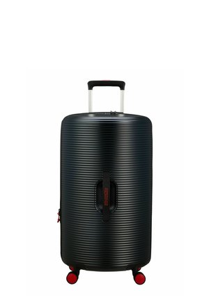 Valise rigide noire avec texture à nervures horizontales, poignée en aluminium extensible et accents rouges sur les roues et le logo de la marque.