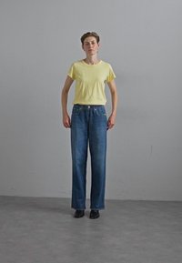 Gul bomull t-skjorte, løs passform, kombinert med høy midje blå denim jeans, rette ben, minimalt med detaljer, brukt med svarte sko.