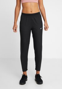 Czarne spodnie sportowe o wąskim kroju, z elastycznym pasem i siateczkowym detalem po bokach. Z przodu znajduje się małe białe logo Nike.