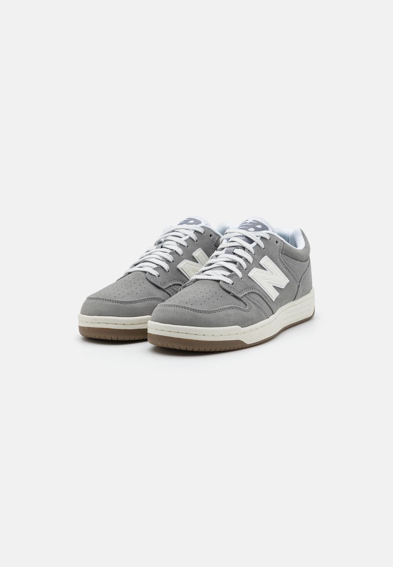 Baskets en daim gris avec des lacets blancs et un logo "N" blanc sur le côté ; tige texturée, semelle en caoutchouc et bout perforé pour la respirabilité.