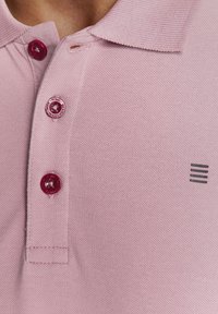 Roze polo shirt met een gestructureerde stof, drie bordeauxrode knopen en een kleine donkergrijze gestreepte accent nabij de zoom.