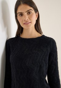 Maglione blu scuro con trama a zigzag, caratterizzato da maniche lunghe e collo tondo. Il materiale sembra morbido e accogliente.