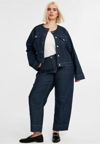 Tummansininen farkkutakki ja housut setti, jossa on kontrastitikkaukset. Rentomallinen, pyöreä kaula-aukko ja etutaskut takissa. Mustat loaferit.