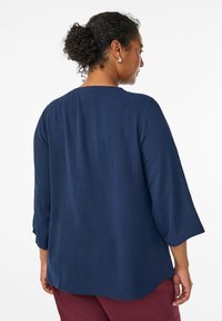 Haut long à manches longues en bleu marine texturé avec un décolleté arrondi et une coupe décontractée, associé à un pantalon bordeaux avec un ourlet incurvé.