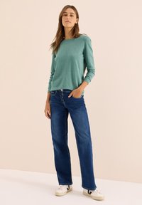 Chemise à manches longues vert clair associée à un jean droit bleu. Baskets blanches avec des accents sombres. Design simple et coupe décontractée.
