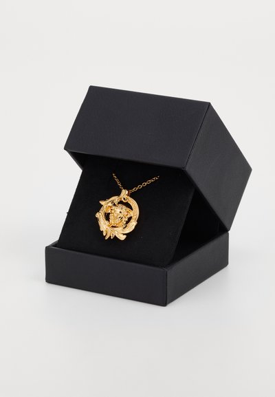 Gold ornate pendant necklace with a Medusa head design displayed on black velvet inside an open black jewelry box.