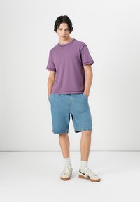 Purple short-sleeve T-shirt with a round neckline, paired with light blue denim shorts. Worn with white and tan sneakers and white socks.