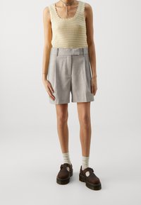 Débardeur en tricot beige clair avec des bords festonnés, associé à un short gris bien ajusté. Les chaussures sont en cuir marron avec une semelle épaisse.