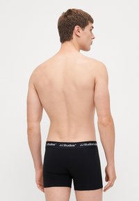 Schwarze Boxershorts aus weichem Stoff mit elastischem Bund, auf dem der Markenname "JJ Studios" in Weiß steht. Das Modell ist von hinten gezeigt.