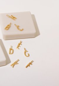 Gyllene alfabetiska bokstavsberlocker arrangerade på en ljus yta, med en slät, glänsande yta och olika versaler synliga.