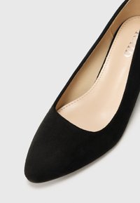 Black suede pump with a pointed toe, a low-cut front, and a smooth, beige leather interior. Minimalistic design, no visible hardware or accents.