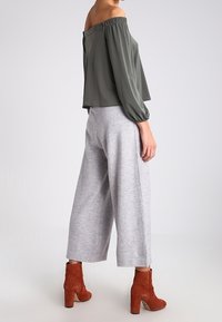 Olijfgroene off-shoulder top met lange mouwen, gecombineerd met lichtgrijze wijde broekspijpen en roestkleurige blokhakken enkellaarzen.