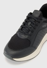 Men's black sneaker with leather and mesh upper, lace closure, perforated accents, and a white rubber sole. Brand logo visible on the side.