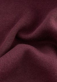 Burgundy stickad tyg med en fin struktur, som visar släta, elastiska trådar och subtila variationer i färgdjup.