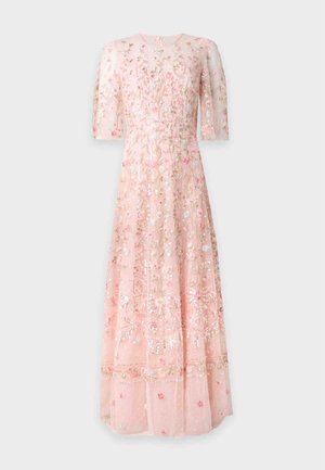 Mujer que lleva un vestido rosa transparente hasta el suelo con bordados florales y mangas cortas, combinado con sandalias de tacón alto abiertas en tono nude.