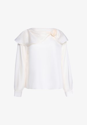 Blouse blanche manches longues avec un large col plié et un détail de rose en tissu sur le côté gauche près de l'encolure.