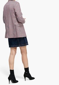 Kraciasta marynarka w czerwono-białym kolorze, zestawiona z ciemną spódnicą dżinsową. Czarne skarpetki do kostki i sandały na otwartym nosku dopełniają strój.