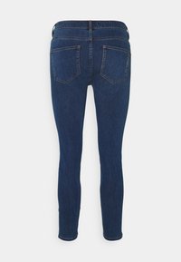 Vaqueros skinny de mezclilla azul oscuro con dos bolsillos traseros y trabillas, mostrados desde la parte de atrás sobre un fondo blanco.