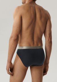 Granatowe slipy z błyszczącą srebrną gumką w talii, wykonane z miękkiego materiału, charakteryzujące się elastycznym krojem i gładkimi krawędziami. Przejrzysty kształt bez wzorów.