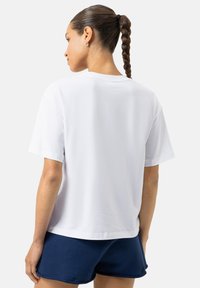 Wit katoenen T-shirt met korte mouwen en een ontspannen pasvorm, gezien van achteren, gecombineerd met marineblauwe shorts. Eenvoudig en veelzijdig ontwerp.