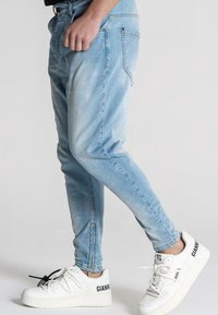 Ljust blå denimjeans med slim fit, som har en urtvättad textur och subtil slitage. Matchas med vita sneakers med svarta detaljer.