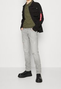 Černá bunda s kapsami, olivově zelené polo tričko, světle šedé džíny s odřenými detaily a černé platformové boty. Hladký a jemný povrch po celém oblečení.