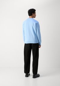 Light blue sweater in soft fabric, featuring a round neck and ribbed edges, paired with black trousers and black shoes.