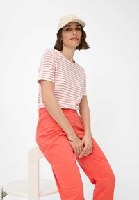 T-shirt a righe a maniche corte in bianco e corallo, abbinato a pantaloni corallo. Gli accessori includono un cappellino beige e un bracciale d'oro.