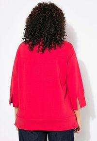 Felpa rossa oversize con maniche a tre quarti, orlo arrotondato e spacchi laterali. Realizzata in un morbido tessuto testurizzato.
