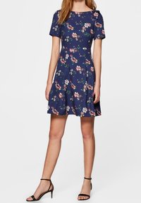 Navy kukkamekko, jossa on lyhyet hihat, istuva vartalo ja levenevä hame. Ominaisuuksia ovat hillitty kukkakuosi eri väreissä ja sileä pinta.