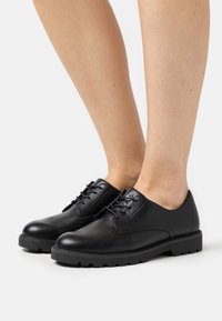 Chaussures en cuir noir au fini lisse, semelle plate et lacets. Comprend des détails de couture subtils et un bout arrondi.