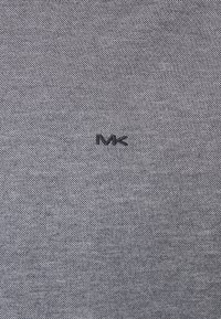 Tela gris con un tejido texturizado, que presenta un pequeño logotipo bordado en negro "MK" en la parte inferior derecha.