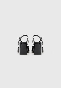 Sandale cu toc din piele patent neagr�ă, cu toc pătrat, curea la gleznă și design cu vârf deschis, evidențiind o textură netedă și lucioasă.