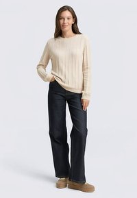 Krém színű bordázott pulóver, laza szabás, kerek nyakkivágással. Sötétkék, bőszárú farmerrel és világosbarna platform cipővel párosítva.