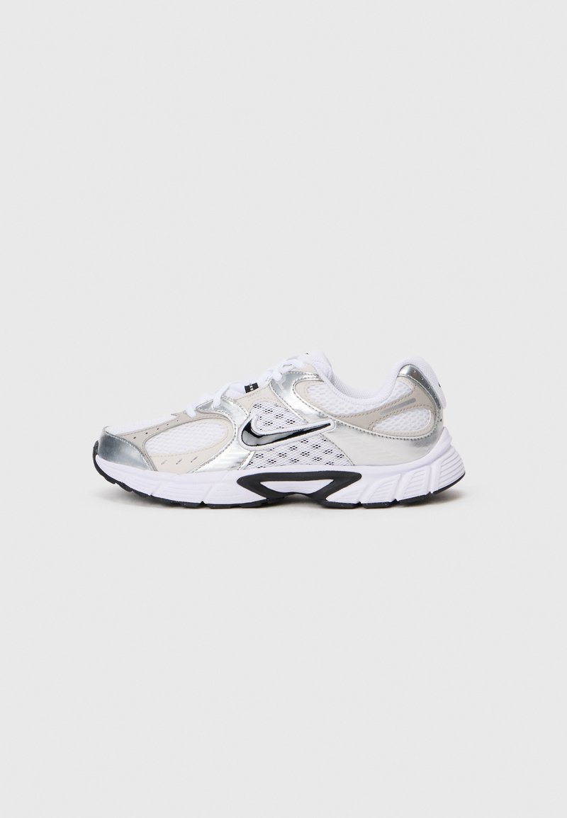 Nike tenisky s bílou síťovinou na svršku, stříbrnými akcenty, černou gumovou podrážkou a podrobným šitím. Obsahují šněrování a logo.