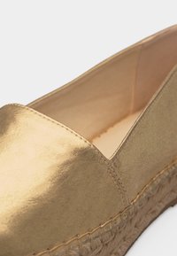 Χρυσό espadrille slip-on με λείο επάνω μέρος και πλεγμένη σόλα από ζούτα με πλατφόρμα, που δείχνει κοντινή λήψη των λεπτομερειών ραφής στα δάχτυλα και την πλευρά.