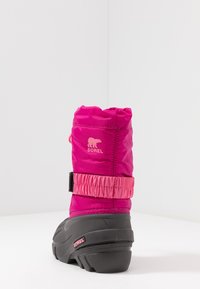 Bota de invierno aislada de color rosa con suela de goma, puño elástico y correa ajustable. Presenta un logotipo en el lateral y una parte superior texturizada.